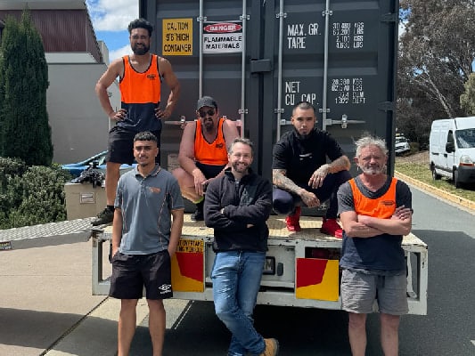 Ontime Movers team members gathered on the back of a flatbed truck in an industrial setting, with high-visibility workwear - capturing camaraderie, readiness, and the hands-on nature of Ontime Movers’ logistics and relocation services.